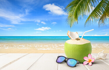 Obraz na płótnie Canvas Coconut juice with sunglass on wooden table with beach and blue sky background.