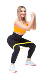 A beautiful, athletic, slim, smiling and cheerful woman in an orange top and black sweatpants performs squats with a fitness band. Lifestyle concept with sports and gym, healthy lifestyle. Isolated on