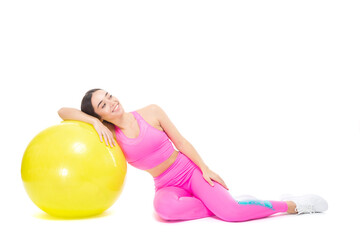 A beautiful, athletic, slim, smiling and cheerful woman in a pink tracksuit sits leaning on a yellow fitball. Rest after stretching or fitness training. Pilates. Lifestyle concept with sports and gym