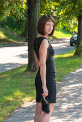 Young girl in black outdoor dress walking in the park in spring. On the background green forest. Perspective of space.