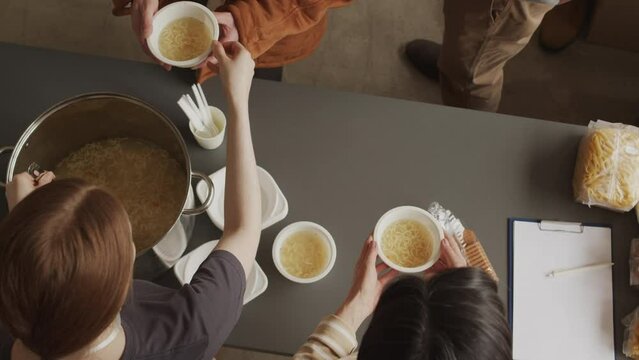 Top view slowmo of two female volunteers pouring soup with instant noodles into disposable bowls providing humanitarian help to refugees, homeless and people in need