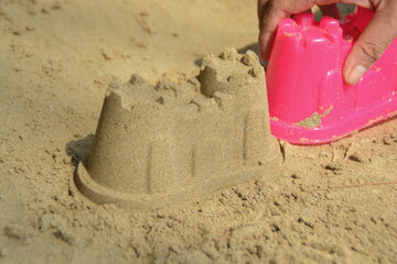 Sand castle on the beach with pink plastic kids toys.