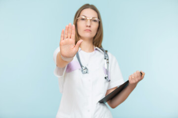 Beautiful woman doctor with a stethoscope and a black tablet, shows a stop sign with her hand, on a blue background. Copy paste. healthcare concept. Let's stop the disease.