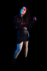 Obraz premium young latin woman dressed in black clothes with colorful red-blue lights on black background in Mexico Latin America 