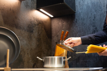 Close-up. A man cooks spaghetti in the kitchen. He dips the pasta into a pot of boiling water.