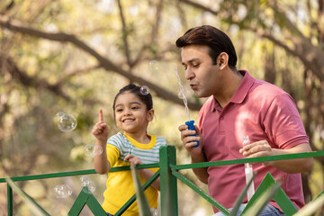 Carefree father and daughter having fun playing with bubble at park