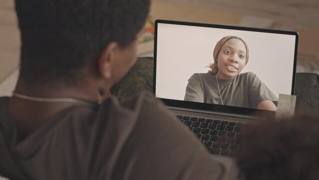 From above slowmo of young Black military woman communicating with her beloved family through video chat on laptop, talking to little daughter and husband sitting on sofa at their home