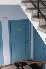 Apartment doors and stairs fragment. Building hall interior with beautiful blue wooden doors and staircase. Classic home entrance with door bells. Span view. Vertical, selective focus