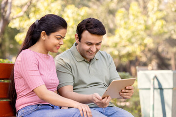 Obraz premium Beautiful couple using tablet at park