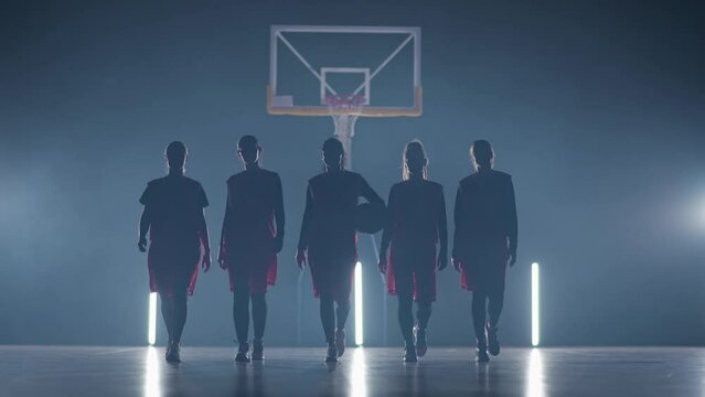 Slow motion performance, team of basketball female players walks through the gym in contour lighting, the international women's basketball championship, team stance in front of the camera.