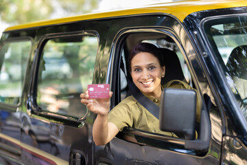 Woman taxi driver showing card sitting inside car