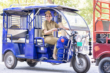 Portrait of happy woman in uniform driving six seater electric rickshaw