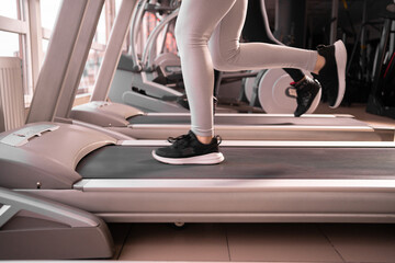 Fototapeta na wymiar Close-up of sneakers female muscular legs while running on a treadmill in the morning