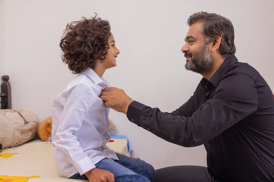 Portrait of father buttoning shirt of his son at home