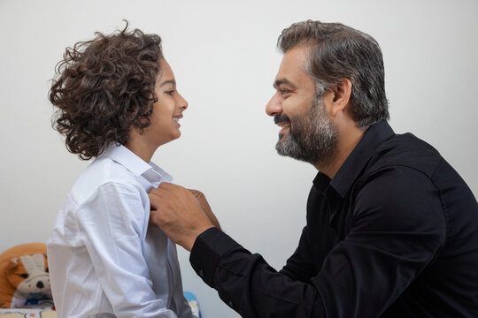 Portrait of father buttoning shirt of his son at home