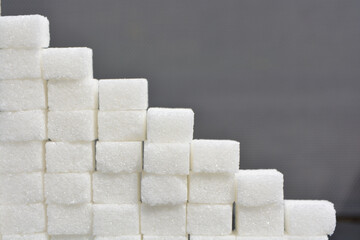 Steps made from sugar cubes. Pile of sugar cubes on a grey shiny surface, sugar pyramid. - obrazy, fototapety, plakaty