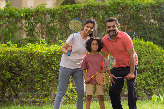 Happy parent with their child posing in front of camera with holding badminton racquets in the park
