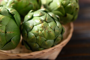 Fototapeta premium Green artichoke in bamboo basket on wooden background, Edible flower bud