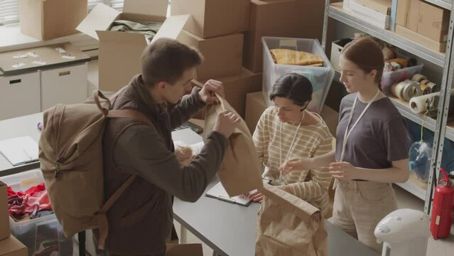 From above slowmo of female volunteers in food bank providing basic provisions to people in difficult situation