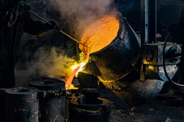 Foundry production. A worker with a special tool stirs the molten metal in a casting ladle