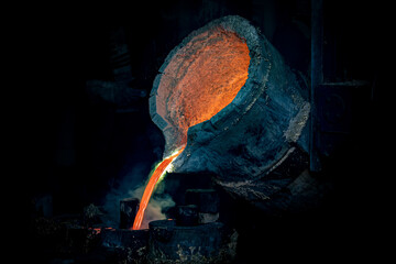 Foundry production. A ladle with molten metal. Pouring hot liquid metal into special molds. Close-up