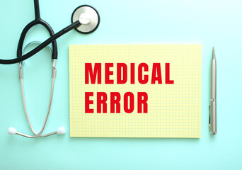 The red text MEDICAL ERROR is written in a yellow pad that lies next to the stethoscope on a blue...