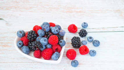 Mix of different berries lie in a heart-shaped plate