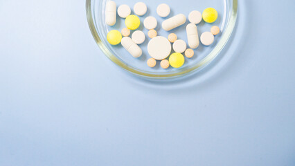 Different multi-colored tablets in a Petri dish on a blue background