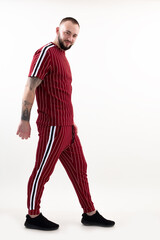 Portrait of young smiling bearded man with short dark hair wearing red striped sport wear, standing on white background.