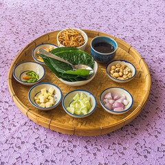 Miang Kham tray filled with raw materials as a cup to eat on the table with a purple patterned tablecloth.