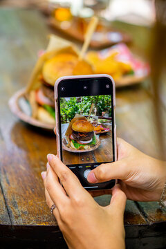 A woman taking a picture of a burger with her smartphone.