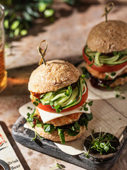 Two delicious homemade burgers of beef, cheese and vegetables on wooden board at greenery background.