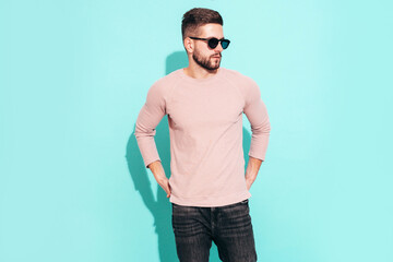 Portrait of handsome confident  model. Sexy stylish man dressed in pink sweater and jeans. Fashion hipster male posing near blue wall in studio. In sunglasses. Isolated