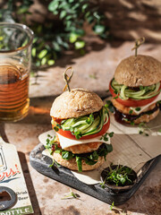 Two delicious homemade burgers on wooden board with beer at greenery background.