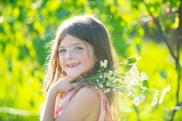 Outdoor small child girl portrait on the meadow. Little cute kid with flowers in a garden. Children play outdoors. Kid play outdoor. Concept of happy childhood and summer leisure.