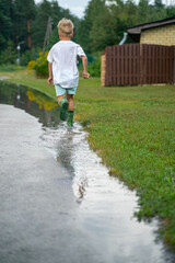 A cheerful child runs through the puddles after the rain on a warm day