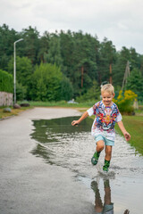 Naklejka premium A cheerful child runs through the puddles after the rain on a warm day