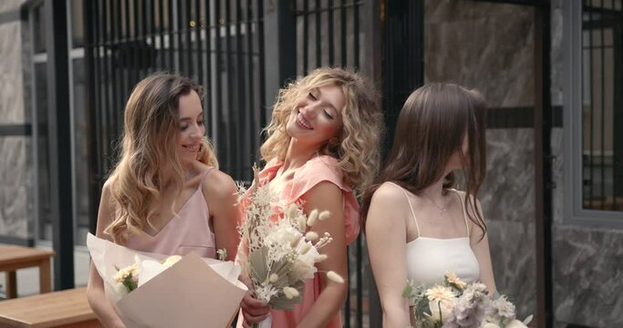 Three hapy ladies with bouquets posing in the city