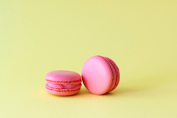 Bright pink macaroons lie on a yellow background. Light yellow background, text space