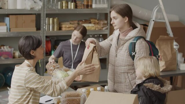 Slowmo of volunteer organization giving humanitarian help to diverse refugees including senior man and single mother with little son, standing in queue for basic provisions at local food bank