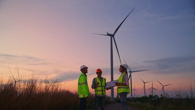 Engineer wearing uniform ,helmet hold document inspection work in wind turbine farms rotation to generate electricity energy. Green ecological power energy generation wind sustainable energy concept