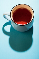 A cup of black tea on blue background under the bright sunlight.