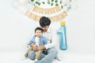 Asian baby boy celebrating first birthday,A father sits and hug his son smiling on a floor with a...