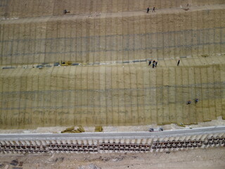 Workers reinforce the slope over the new road. Road construction in progress on slope nature canyon. Infrastructure development and logistics. Aerial drone shot