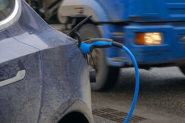 Charging an electric car against the background of a moving large car with the headlight on.