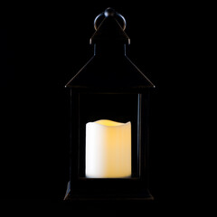 An antique lantern with a candle in a dark key on a black background. Light from a candle. Outlines of the subject