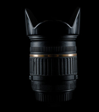 Photographic equipment, photo lenses. One universal zoom lens with an open lens hood stands upright. Side view on a black background