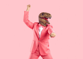 Lustiger, selbstbewusster Mann mit Gummi-Dinosaurier-Maske, der bei Shows oder Veranstaltungen tanzt. Fröhlicher verrückter T-Rex-Typ in funky pinkfarbenem Partyanzug mit Fliege, der Gangnam-Style-Moves macht, isoliert auf pinkfarbenem Hintergrund