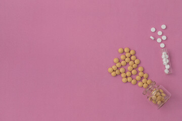 Medicine pills in glass flasks on a pink surface with copy space. Flat lay of white and yellow vitamins scattered on a structural background of glass transparent bottles with space for text.
