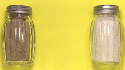 Salt and pepper in salt shakers. separately. On a yellow background. Close up.